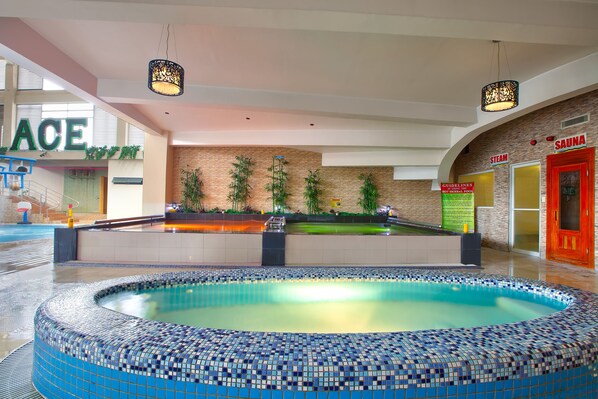 A large indoor swimming pool with a tiled edge, surrounded by a lounge area with seating and plants. - Ace Hotel & Suites (Pasig)