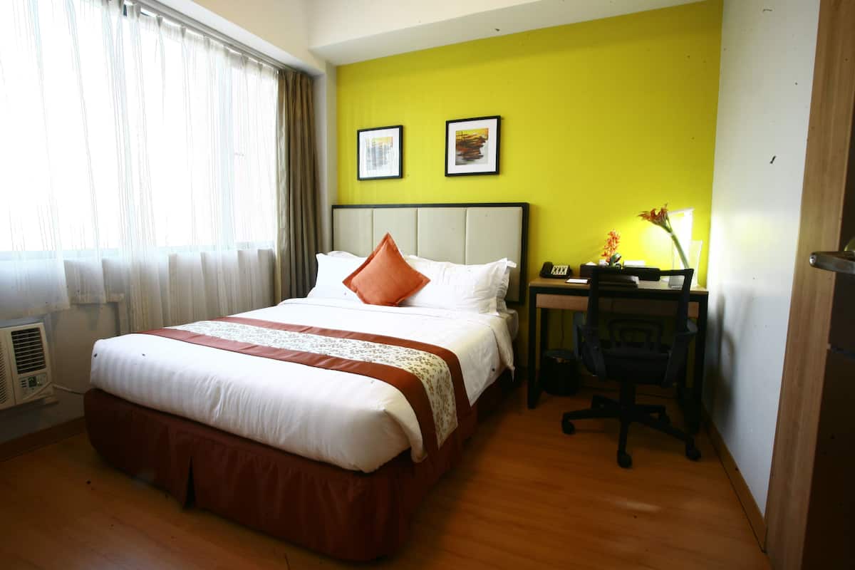 Ein Hotelzimmer mit einem Bett, einem Schreibtisch und einem Stuhl. An der Wand hängen zwei gerahmte Bilder.