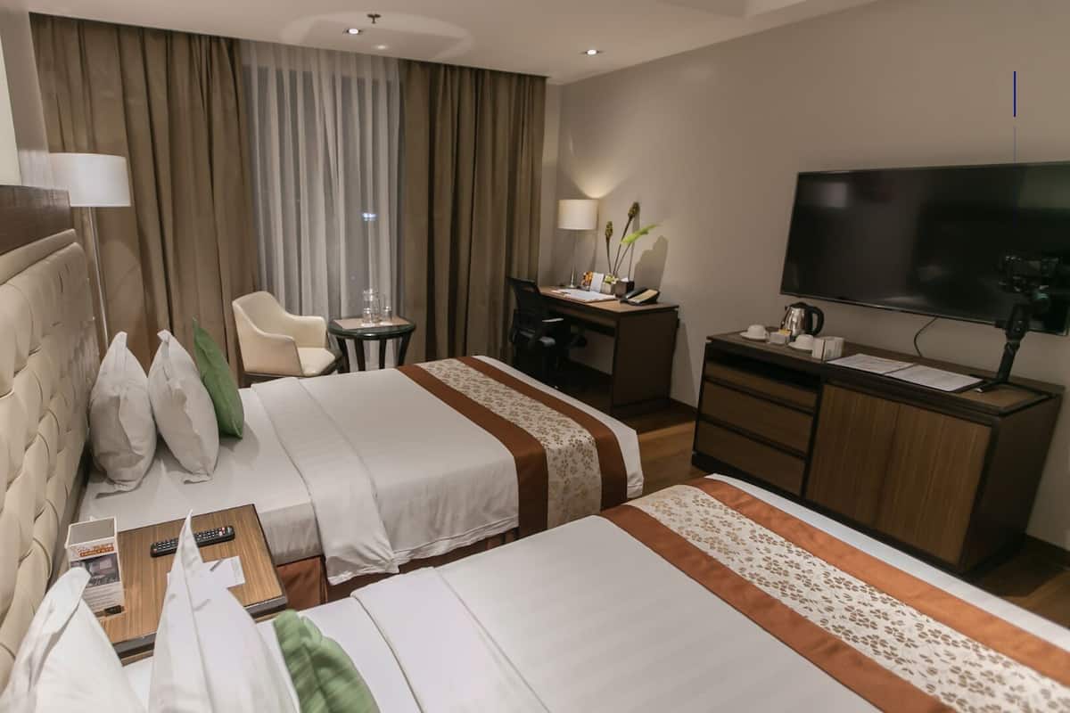 Ein Hotelzimmer mit zwei Betten, einem Schreibtisch, einem Stuhl, einem Fernseher und einem Fenster mit Vorhängen.