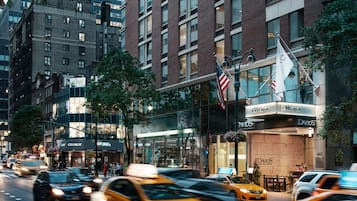 A busy urban street with modern buildings, including a boutique hotel with a glass facade and outdoor seating.