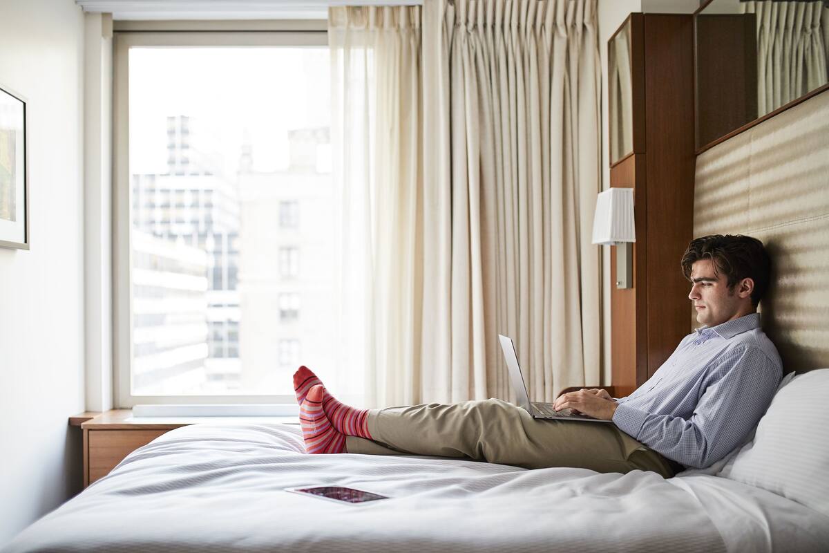 Une chambre d’hôtel avec un lit, un ordinateur portable et une fenêtre avec des rideaux.