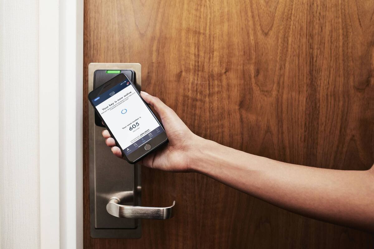 Une main tenant un smartphone près d’une serrure de porte, l’écran affichant un message indiquant qu’une clé est active.