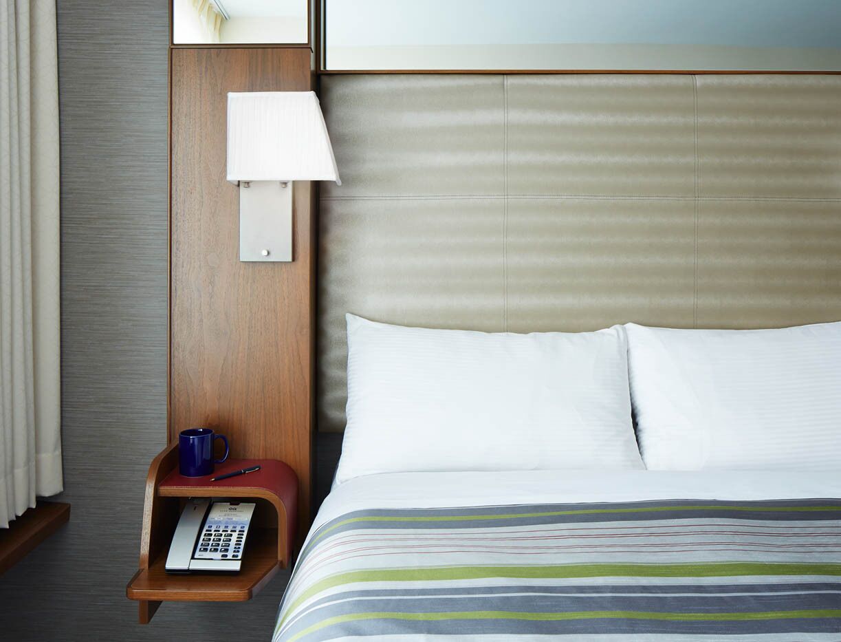 A hotel room with a bed, a nightstand with a lamp, a telephone, and a blue mug.