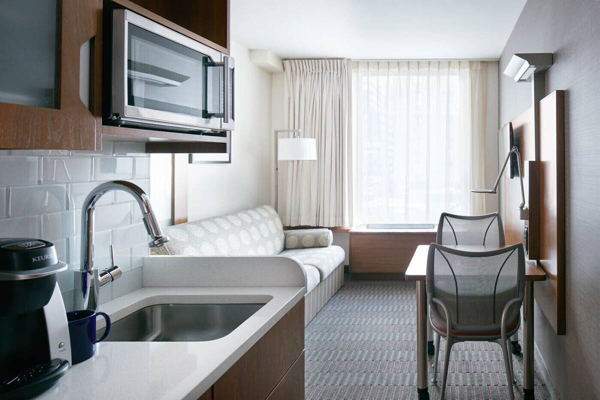 Une chambre d’hôtel compacte comprenant un coin cuisine, un canapé, une petite table et une chaise.