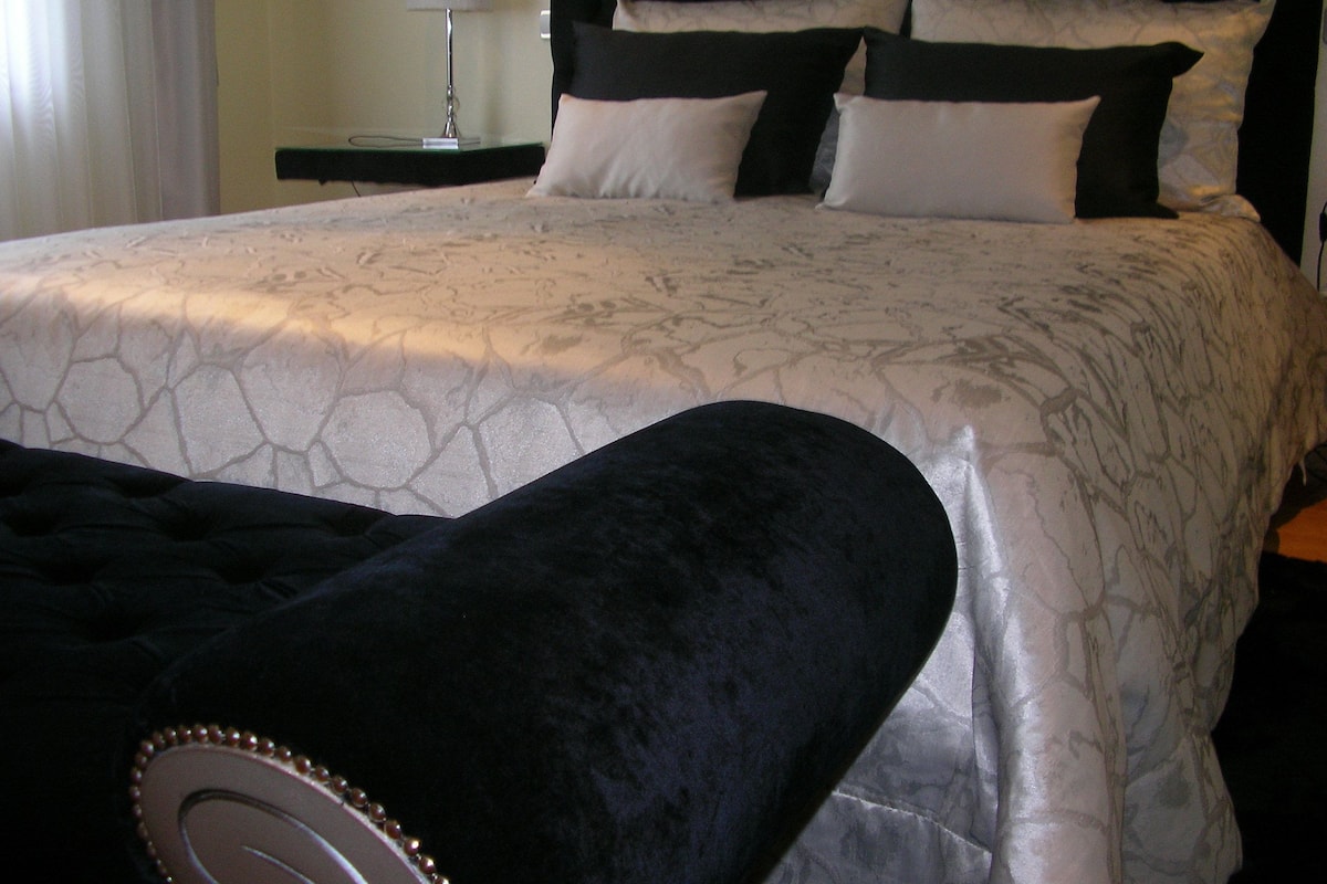 Een bed met een beddekleed met een patroon, een zwart hoofdeinde en meerdere kussens.