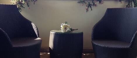 Two wicker chairs and a small round table with a flower on a balcony with a wall covered in greenery.