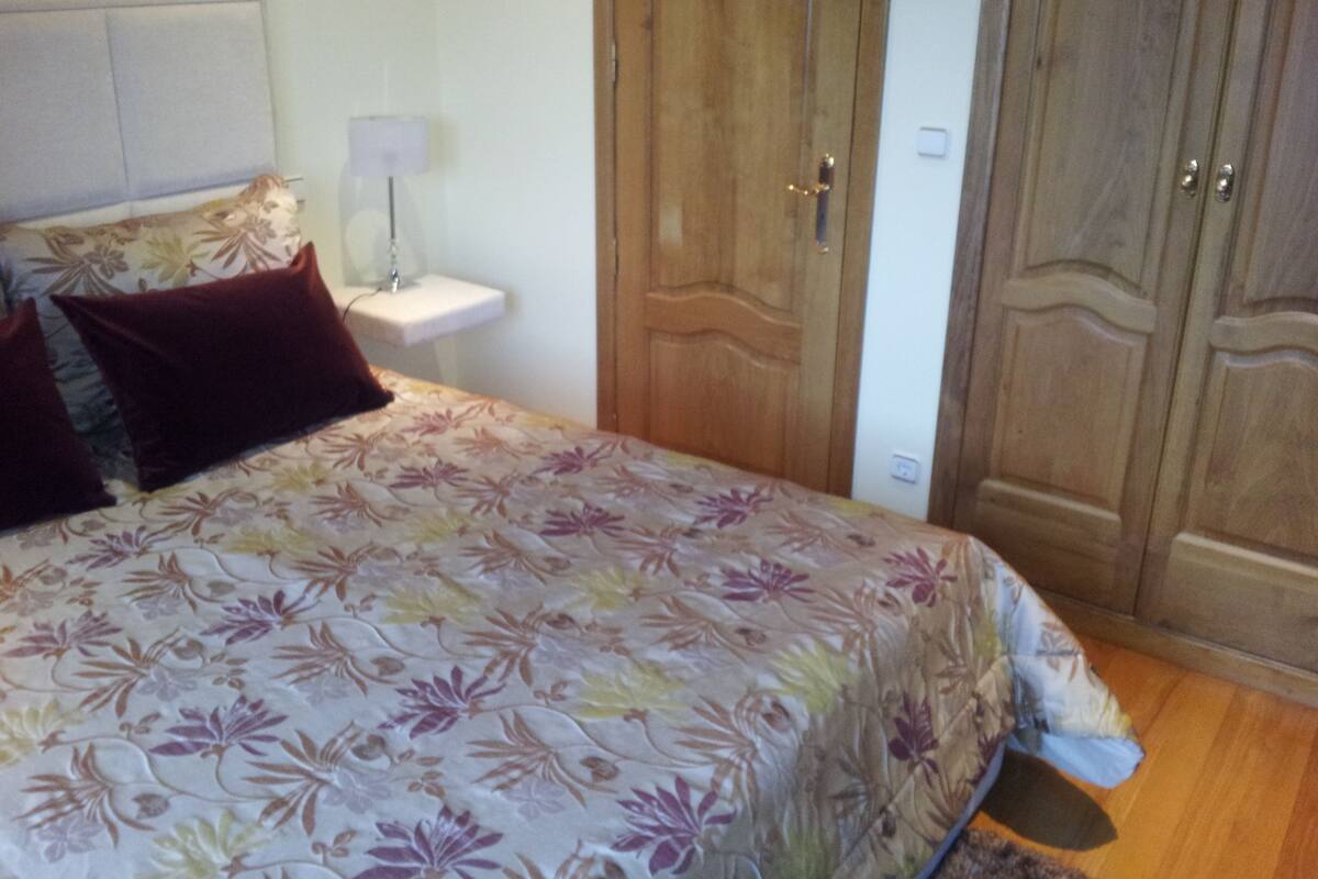 Een slaapkamer met een bed, nachtkastje, lamp en houten garderobedeuren.