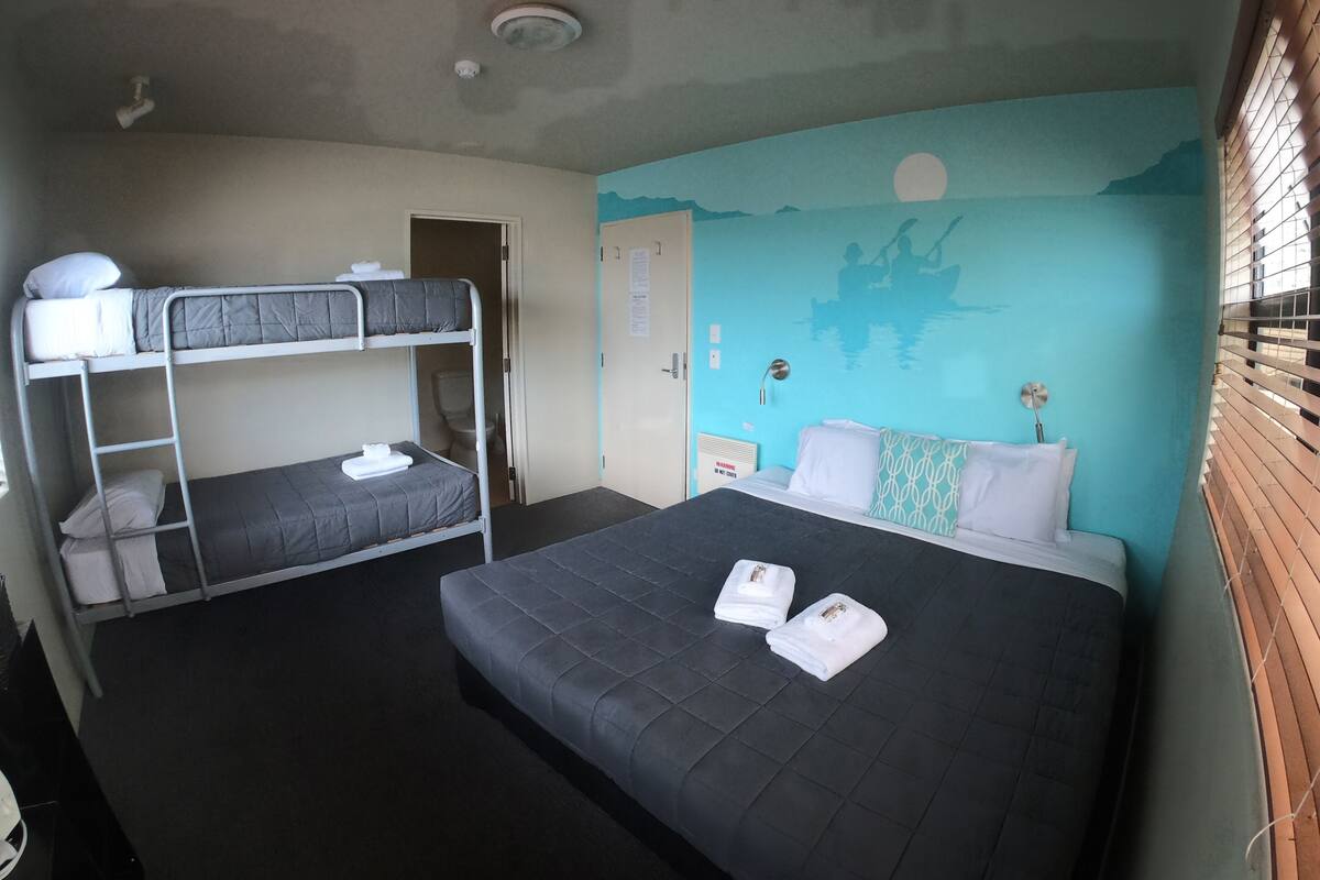 A room with bunk beds, a single bed, a wall mural, a window with blinds, and a door.