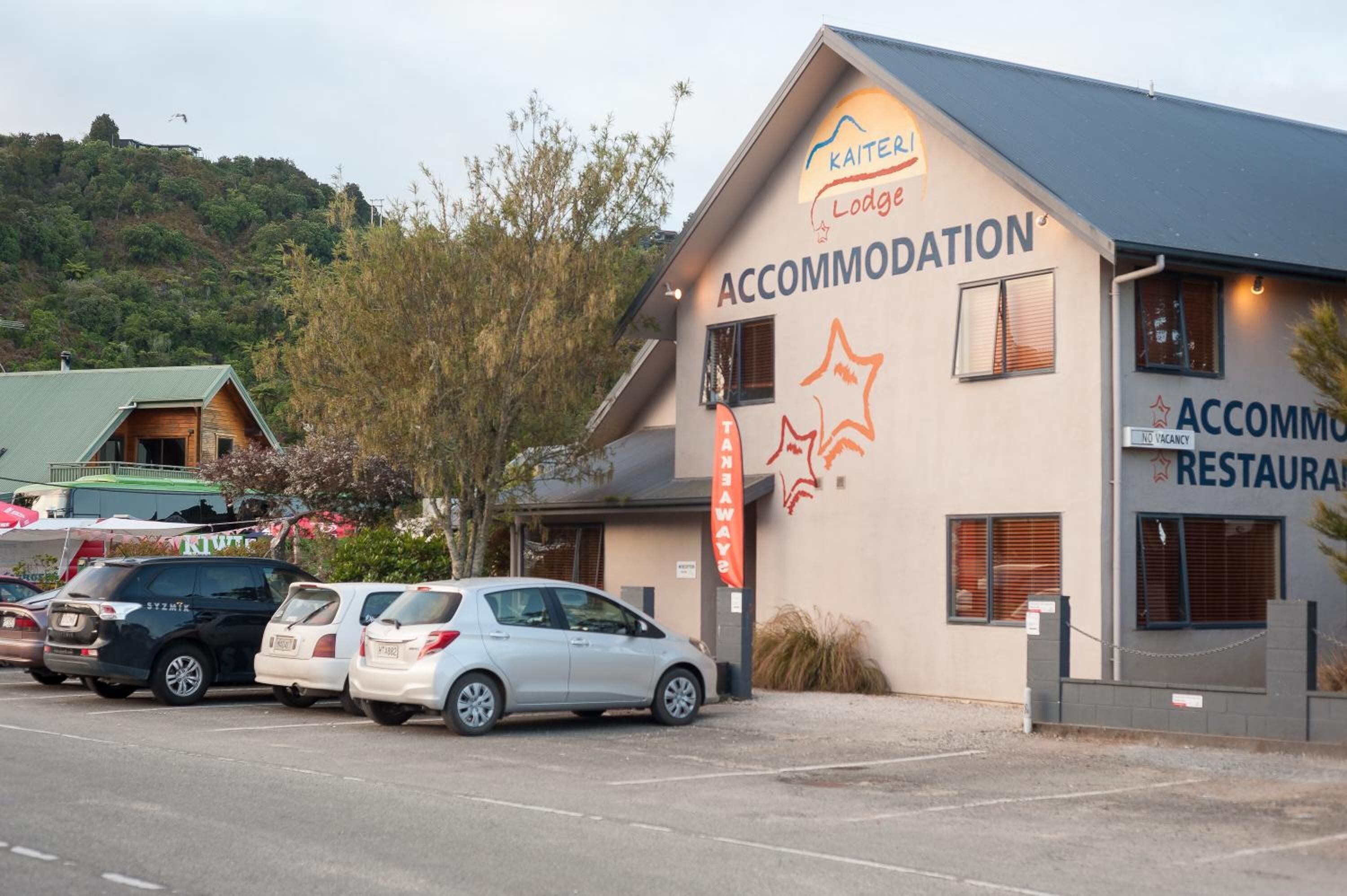 Een gebouw met een bord waarop 'Kaitei Lodge Accommodation' staat en een restaurant. Er staan auto's voor geparkeerd.