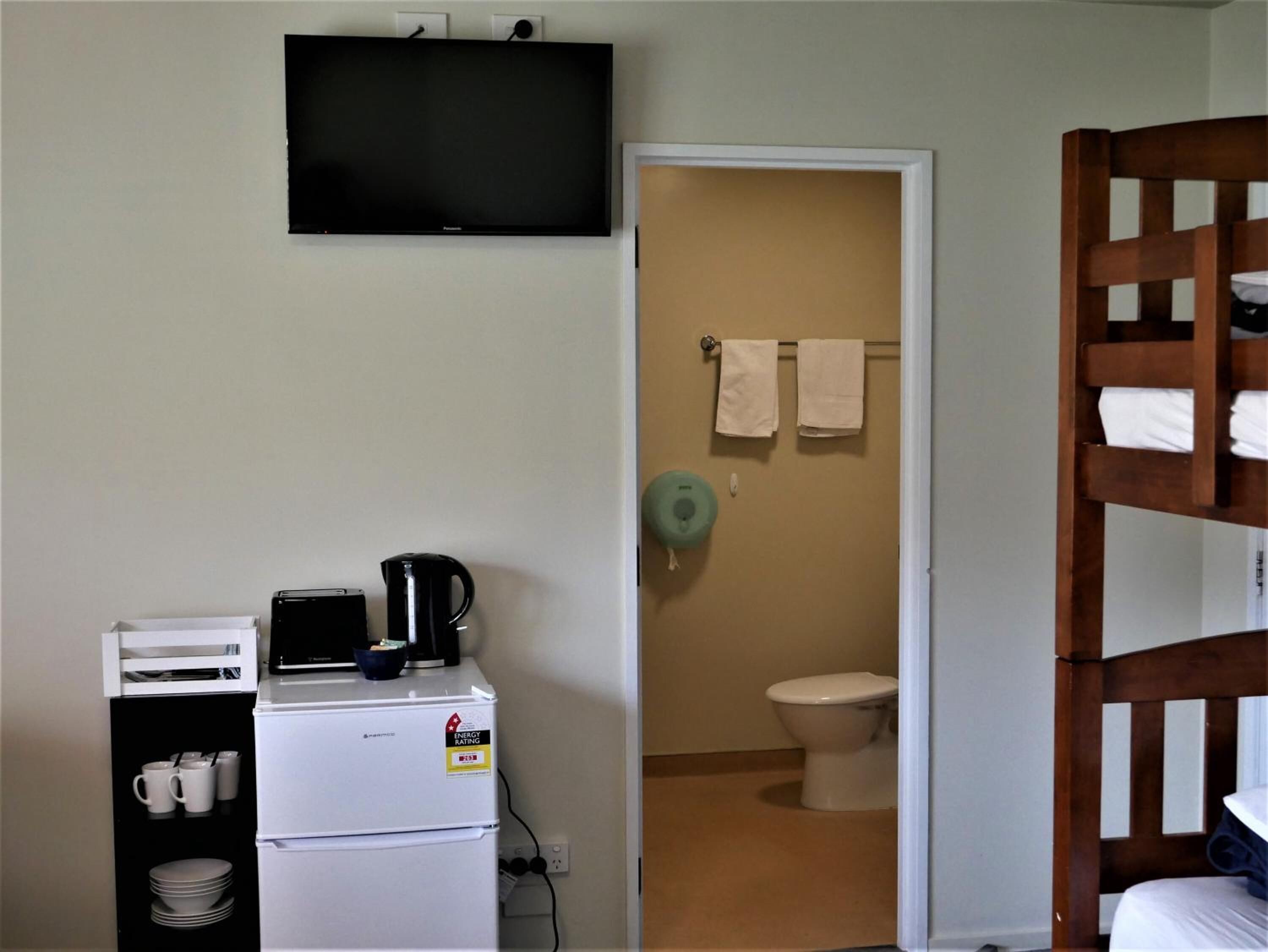 Une petite pièce comprenant un coin cuisine, des toilettes et un téléviseur fixé au mur.