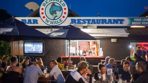 Un bar restaurante con mesas al aire libre, un logotipo de ballena y una pantalla de televisión.