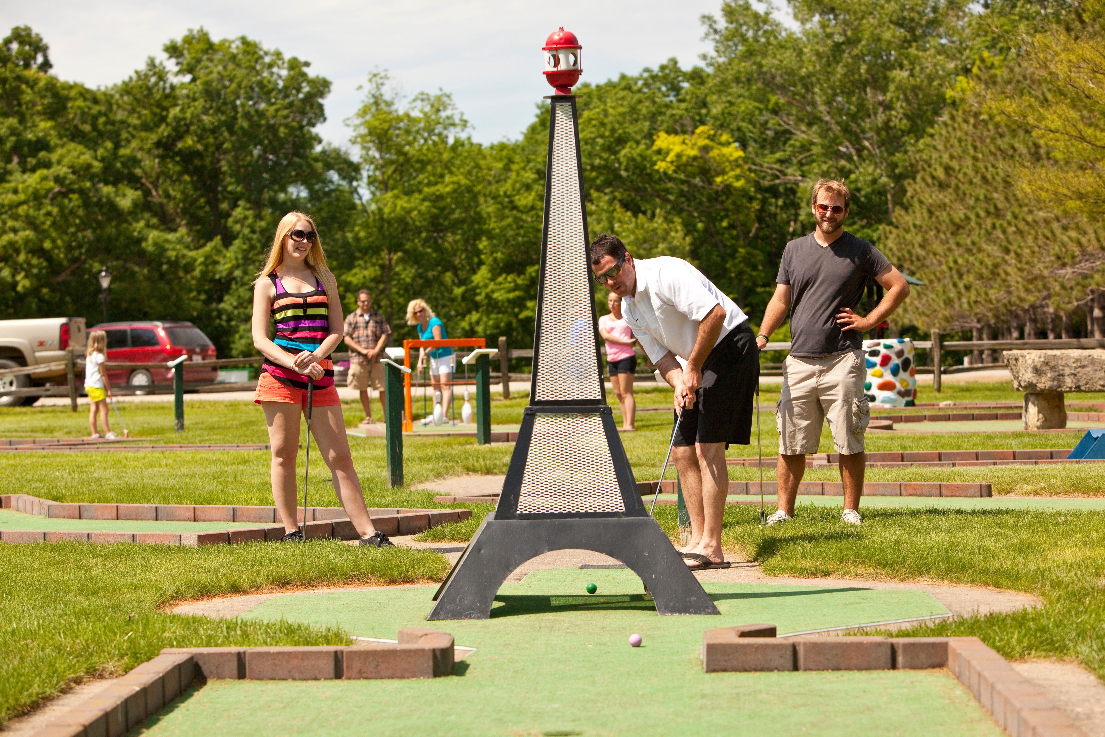 Ein Minigolfplatz mit einer markanten Löcher-Attraktion im Stil des Eiffelturms, umgeben von Rasenflächen und Bäumen.