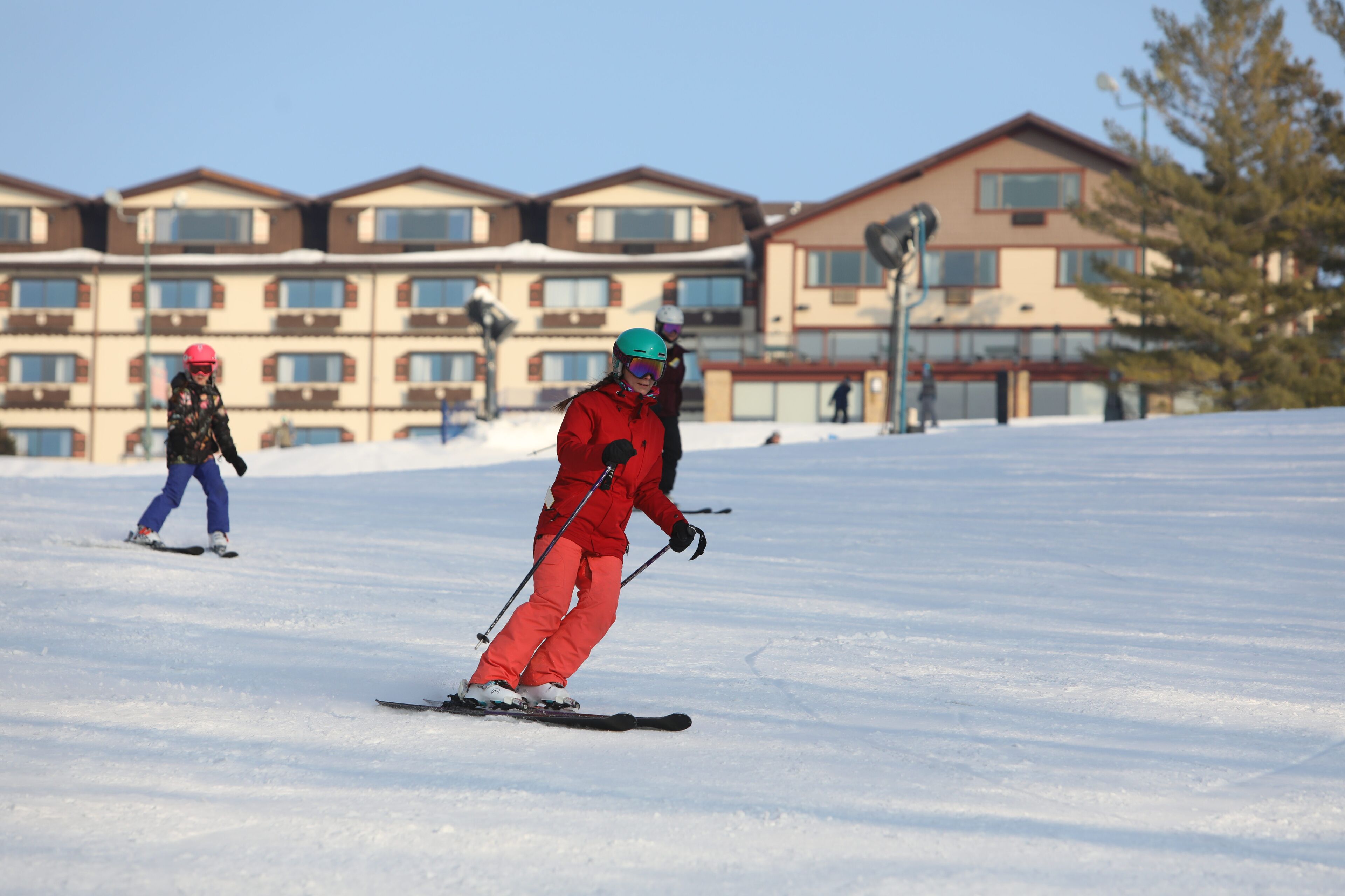 Een piste met een skiënd persoon op de voorgrond en een complex van gebouwen op de achtergrond.