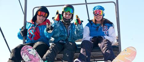 Trois personnes assises sur un télésiège, vêtues d’habits d’hiver et tenant des planches de snowboard.