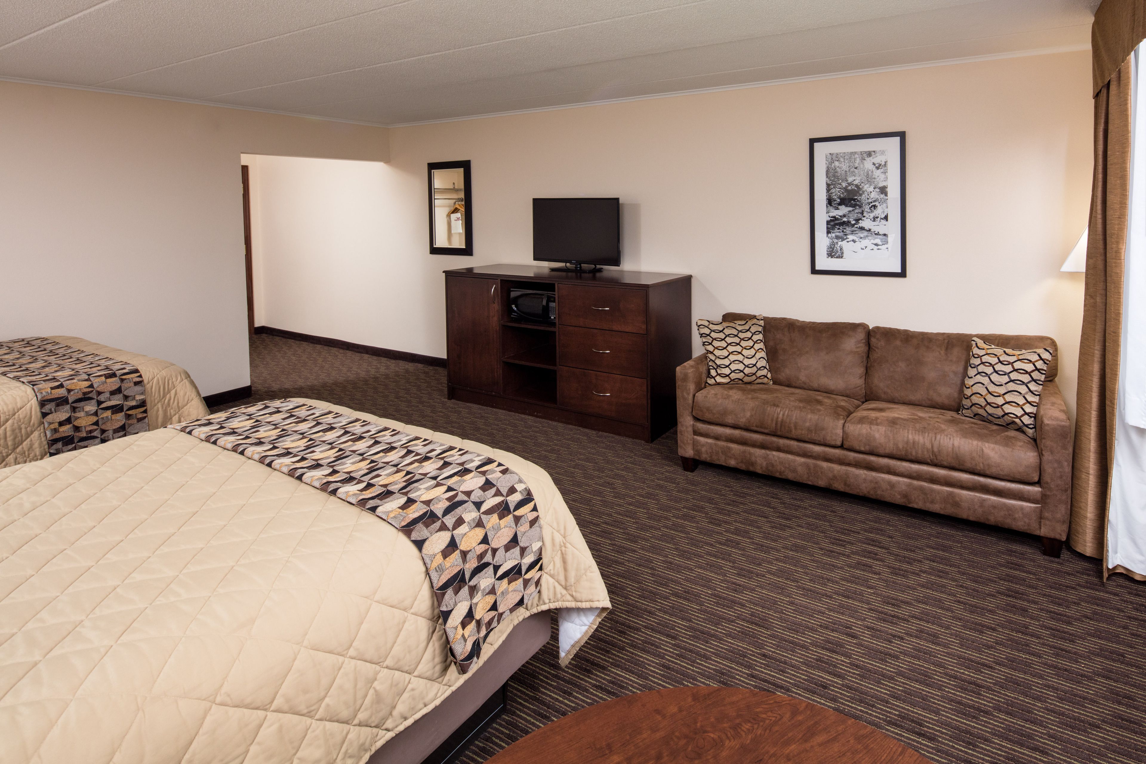 A hotel room with a large bed, a sofa, a TV, and a framed picture on the wall.