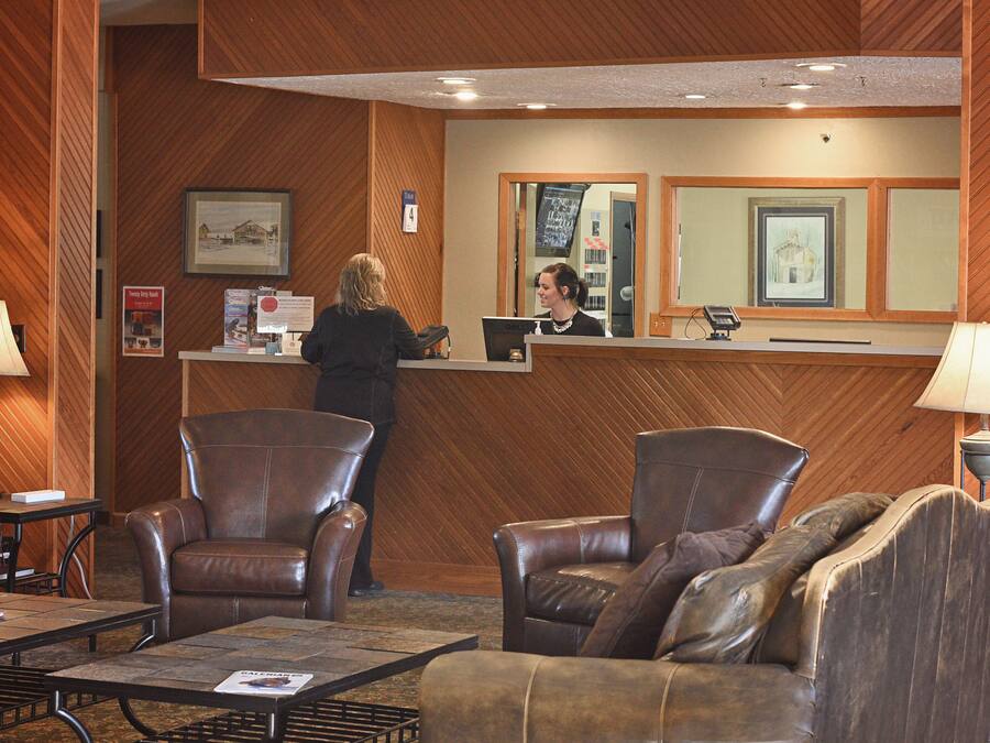 A reception area with a wooden wall, two leather chairs, a sofa, and a reception desk with a computer.