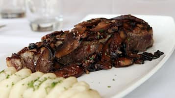 Un plato con un bistec y puré de papas, una copa de vino tinto y una copa de vino blanco sobre una mesa.