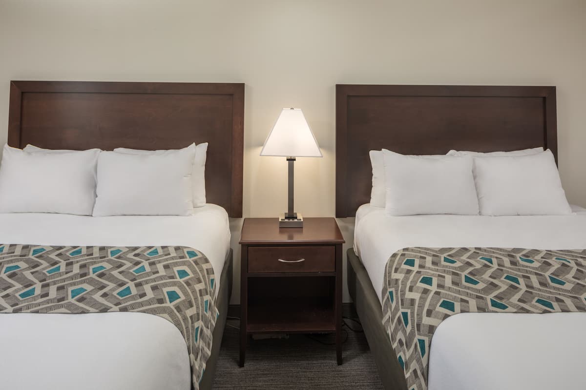 A hotel room with two beds, a nightstand with a lamp, and a patterned bedspread.