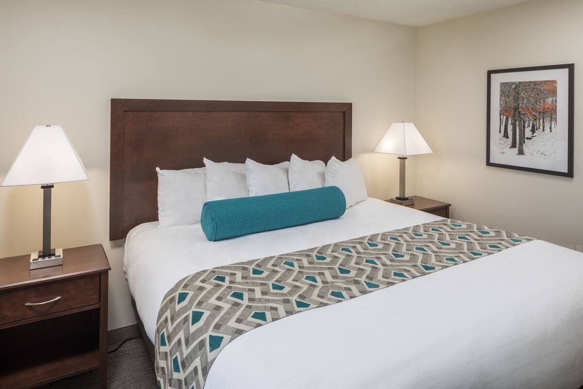 A neatly made bed with a patterned bedspread, two bedside lamps, and a framed picture on the wall.