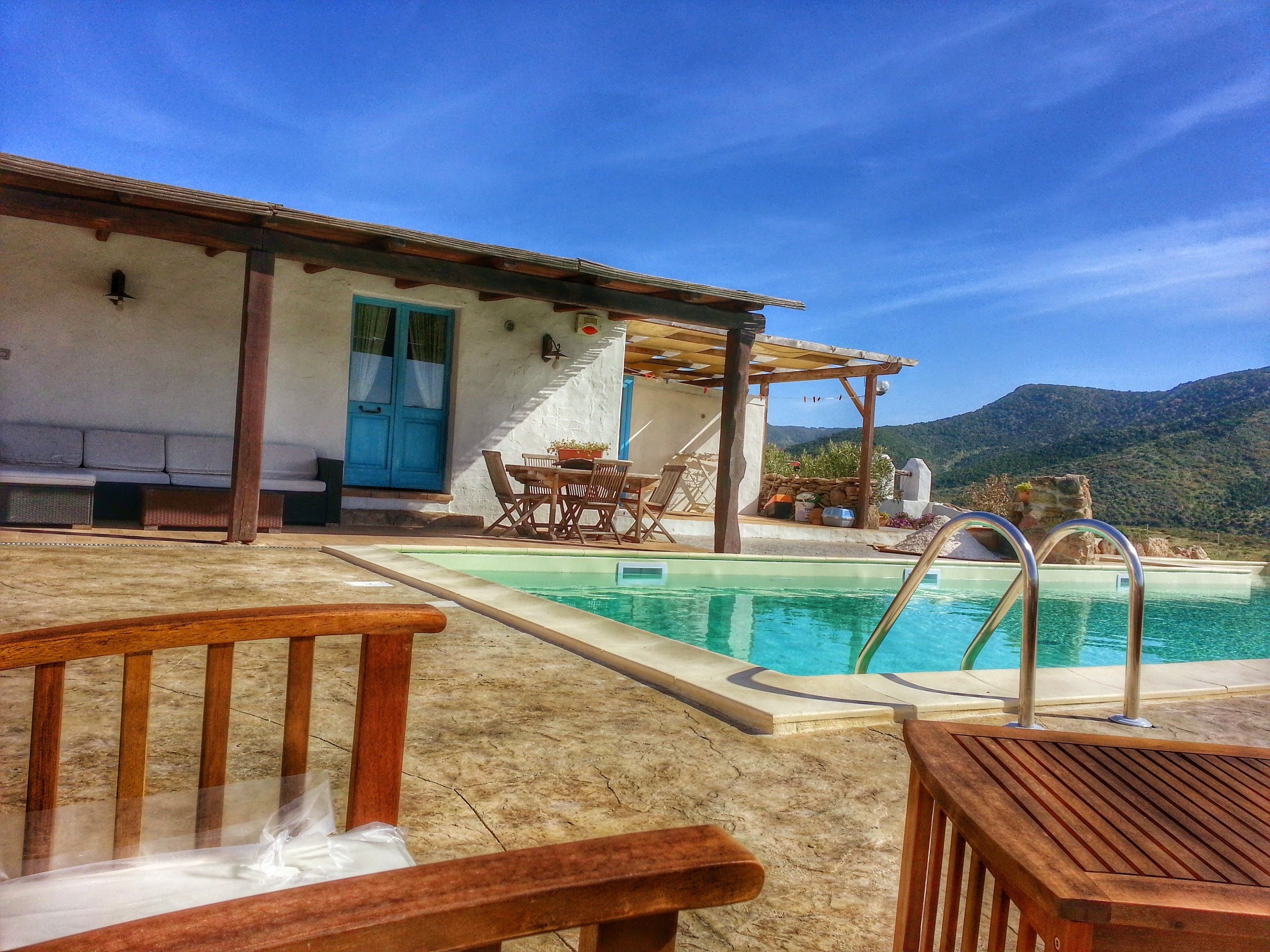 A pool area with a wooden deck, a pergola, and a view of mountains.