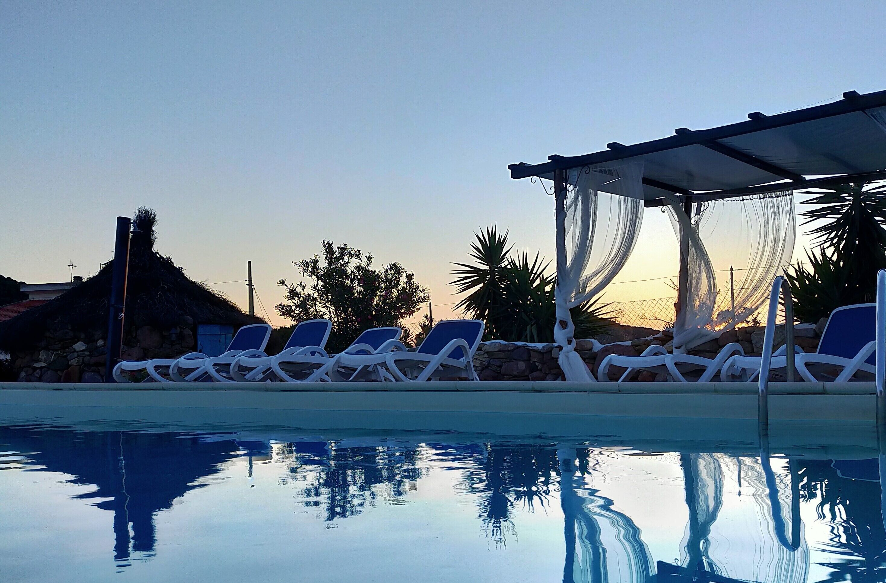 Un área junto a la piscina con sillones de descanso y una sombrilla.