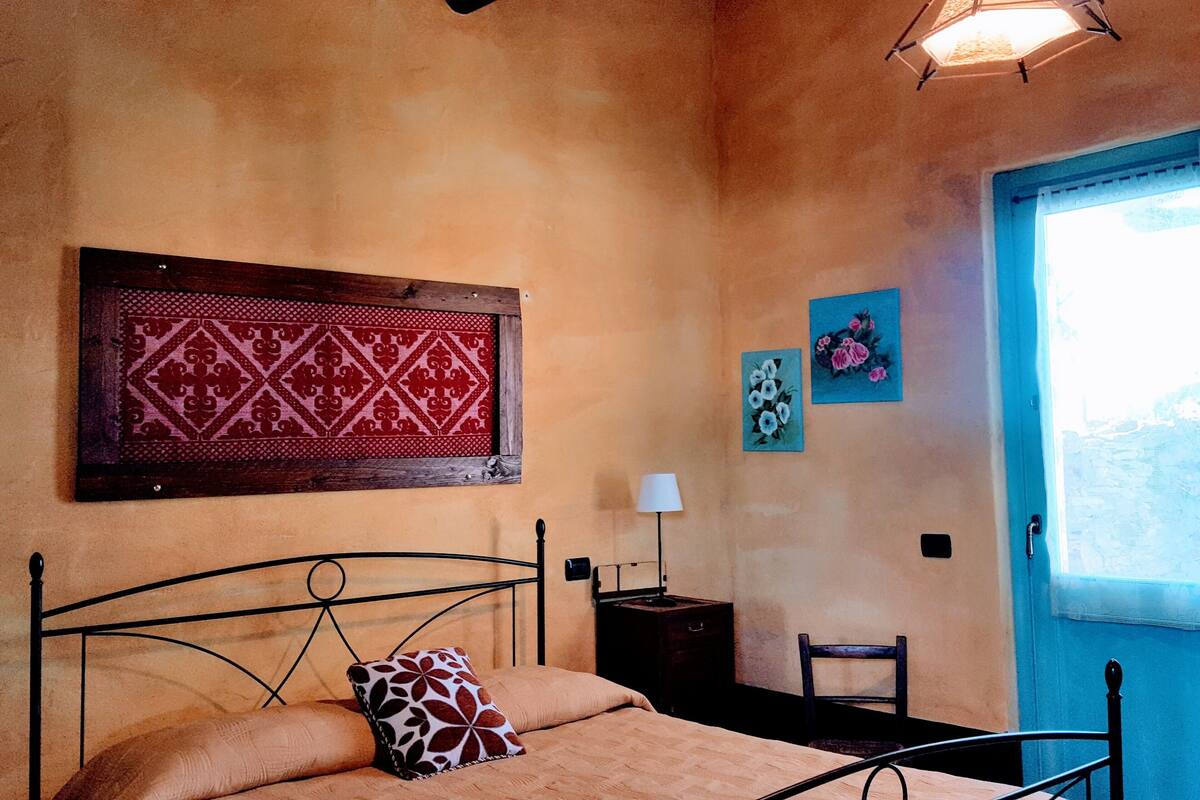 Ein Schlafzimmer mit Bett, Nachttisch, Stuhl, Fenster und Wandbildern.