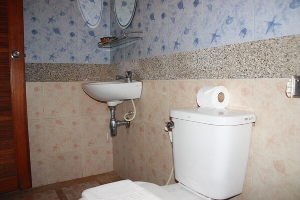 A bathroom with a sink, toilet, and a roll of toilet paper on the wall. - Amorn Mansion (Krabi)