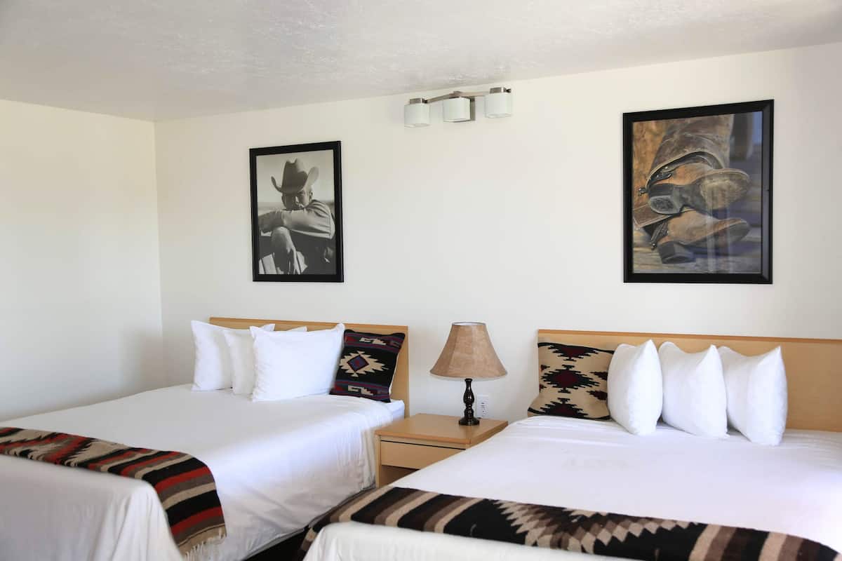 A hotel room with two beds, a nightstand with a lamp, and two wall-mounted light fixtures.