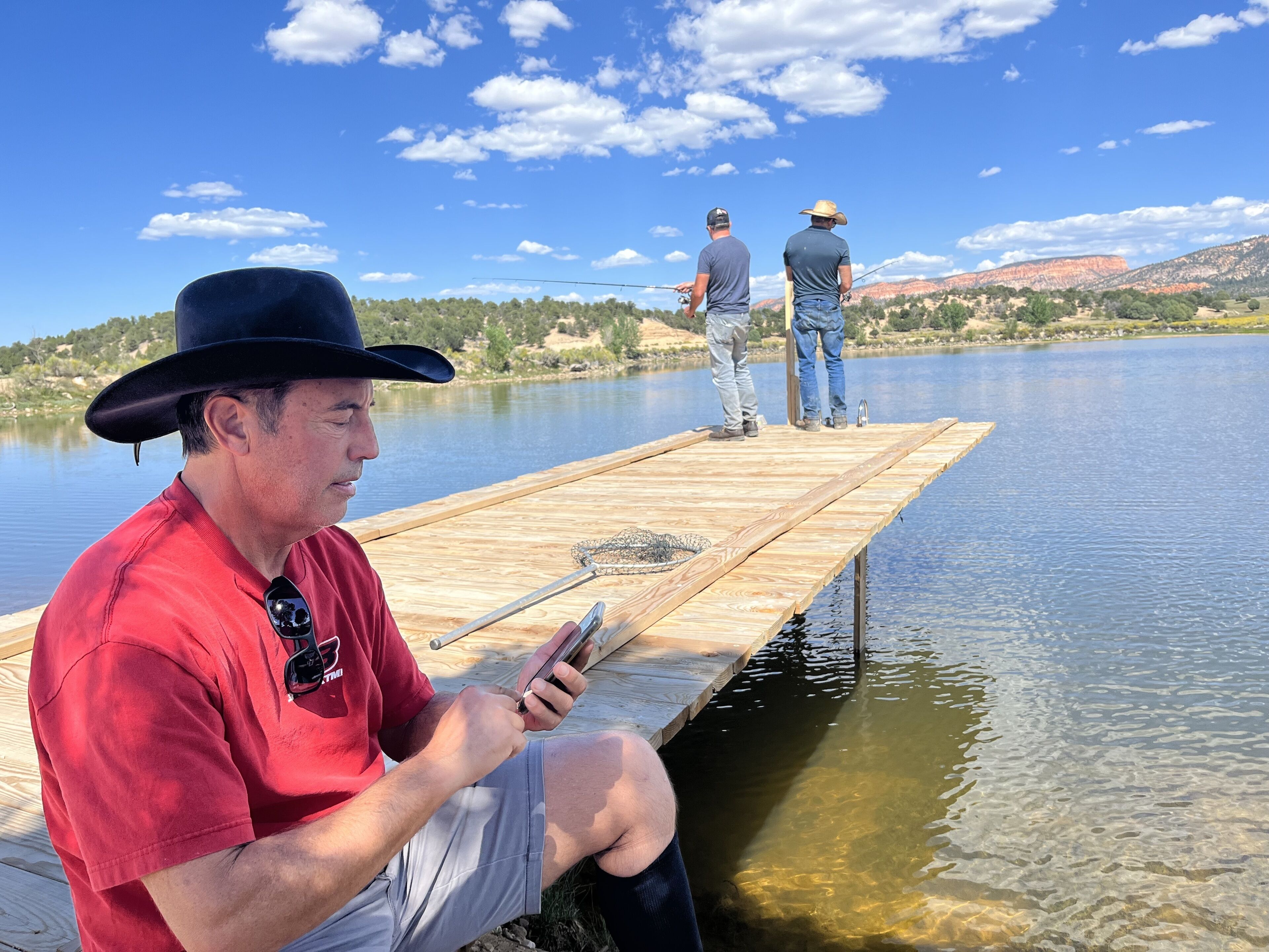 A wooden dock extending into a calm lake with clear water, surrounded by a hilly landscape.