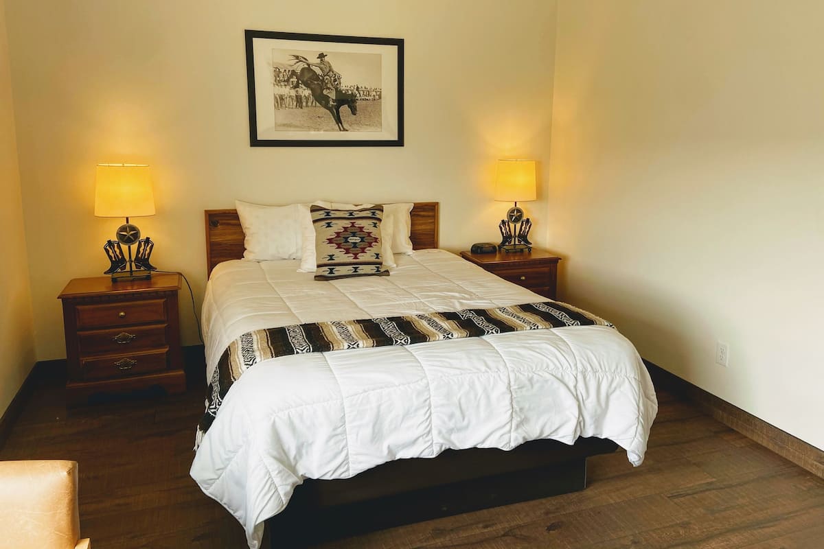 A neatly made bed with a white comforter and patterned pillows, two bedside tables with lamps, and a framed picture on the wall.