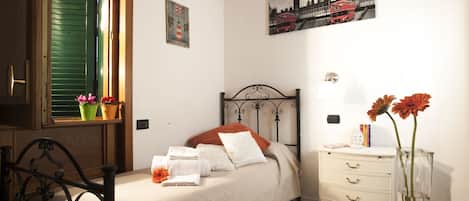 A neatly arranged bedroom with a bed, bedside table, and a window with potted plants.