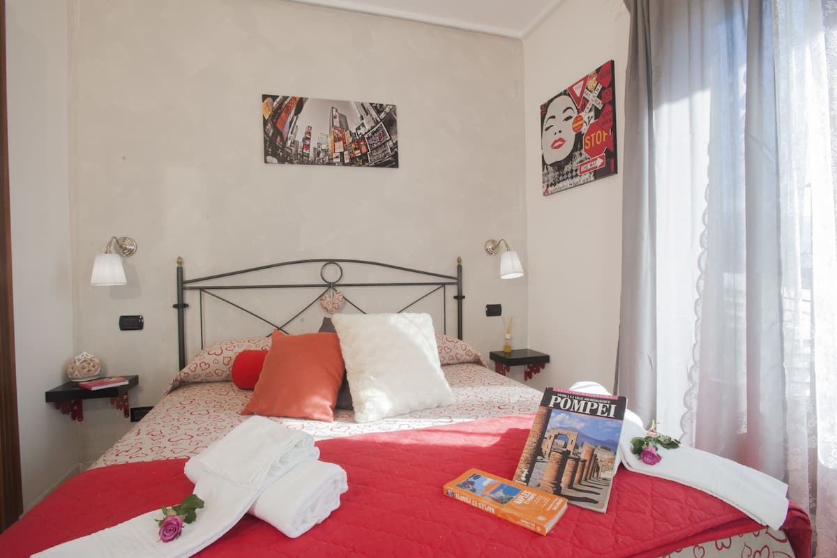 Una cama bien hecha con una colcha roja, almohadas y un libro titulado 'POMPEI'.
