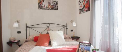A neatly made bed with a red bedspread, pillows, and a book titled "POMPEI".