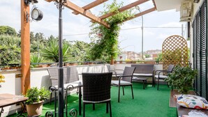 An outdoor patio with wicker furniture, a green artificial turf floor, and potted plants. - B&B Elena (Pompei)