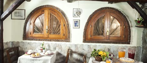 A rustic dining area with stone walls, wooden beams, and arched wooden cabinets.