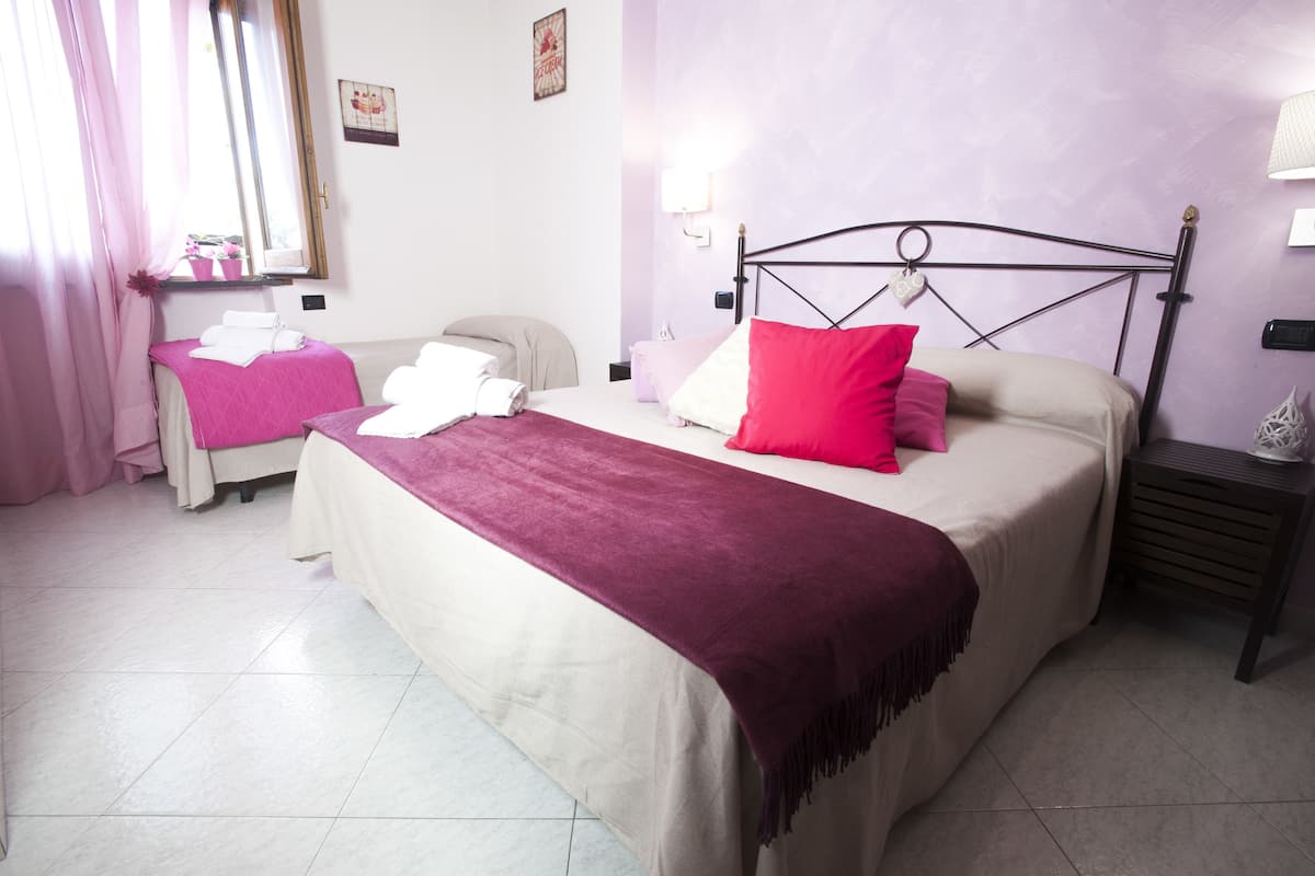 Un dormitorio con una cama, una silla, una mesita de noche, una lámpara y una ventana con cortinas.