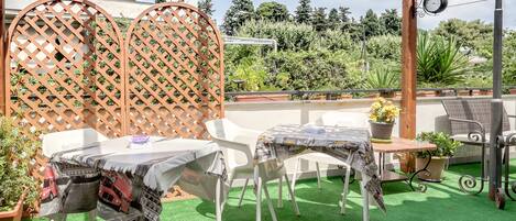 A patio with a table and chairs, covered with a newspaper tablecloth, surrounded by potted plants and a wooden lattice fence.