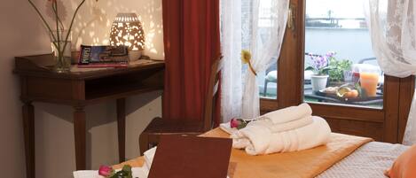 A neatly made bed with a laptop, a vase with flowers, and a lamp on a bedside table.