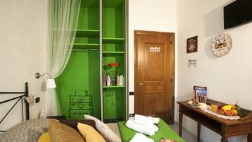 Een slaapkamer met een groene garderobe, een houten deur, een nachtkastje met handdoeken, een klok en een fruitmand.