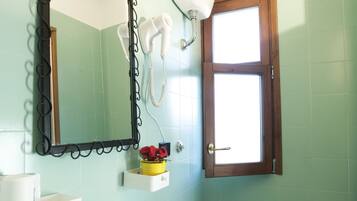 A bathroom with a sink, toilet, mirror, and a window.