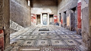 An ancient Roman bath with a mosaic floor, stone walls, and a central doorway. - B&B Elena (Pompei)