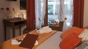 A neatly made bed with a laptop, a bedside table with a book and flowers, and a view of the outdoors through sheer curtains. - B&B Elena (Pompei)