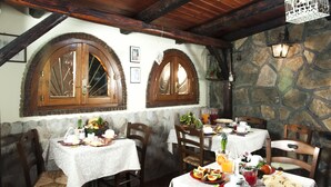 A rustic dining area with stone walls, wooden beams, and arched windows. Tables are set with plates, cutlery, and various dishes. - B&B Elena (Pompei)
