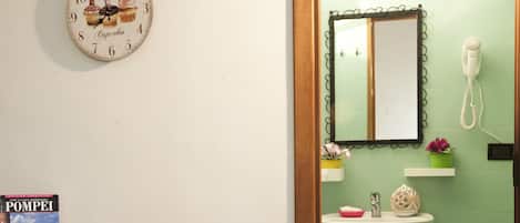 Una habitación con una cama, una mesita de noche con un libro, un reloj, un lavabo y un espejo.