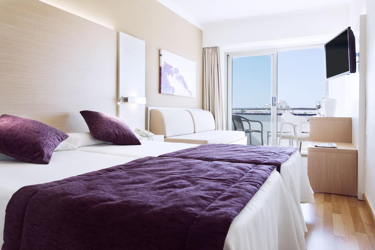 A hotel room with two beds, a TV, a desk, and a balcony with a view.