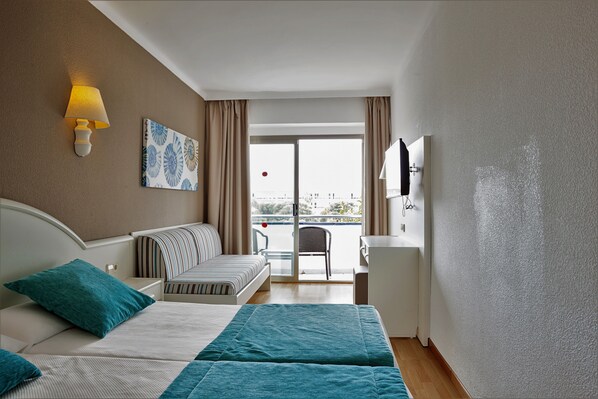 A hotel room with a bed, a desk, a chair, a TV, and a balcony with a view.