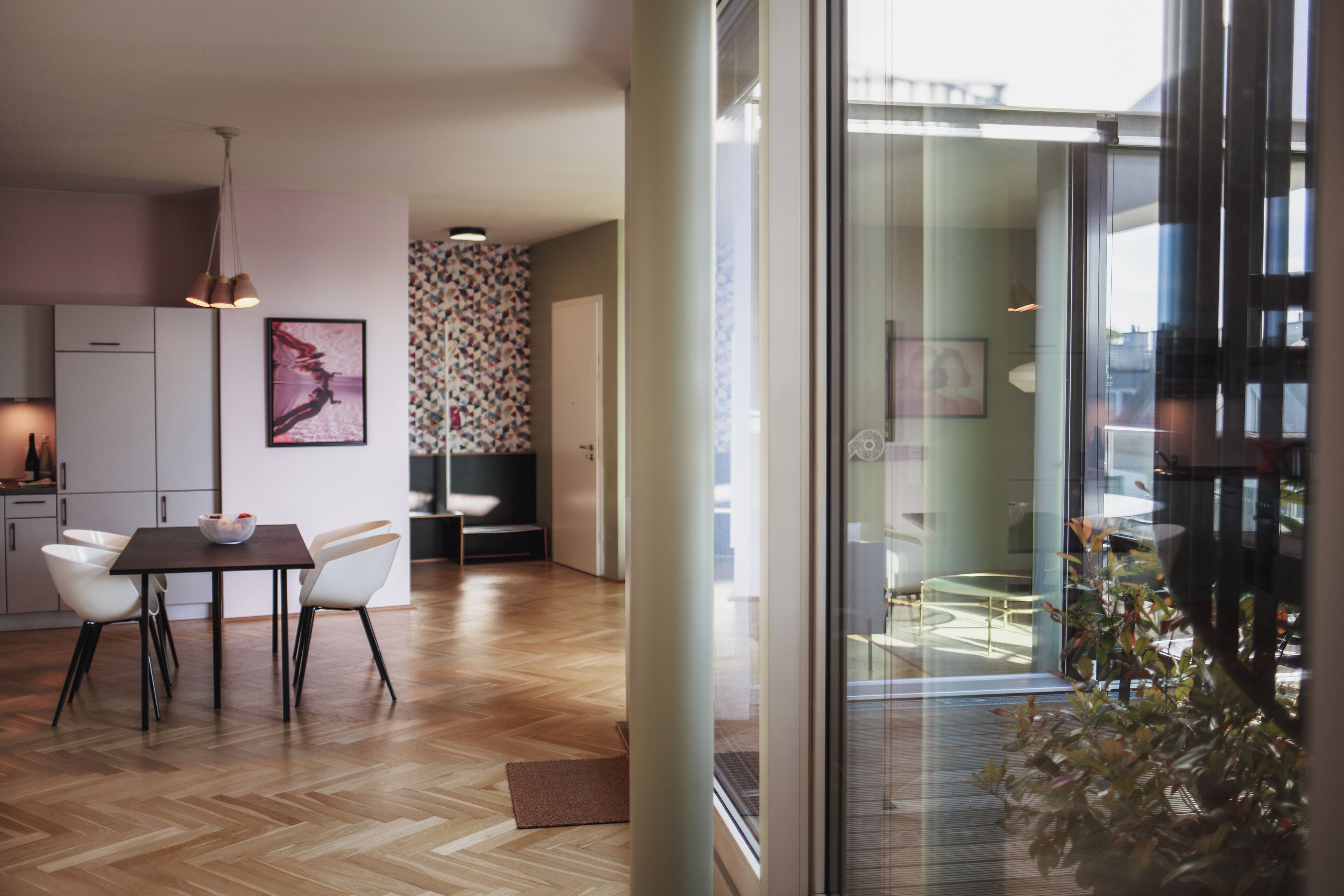Eine moderne Küche mit weißen Schränken, einem Esstisch mit Stühlen und einem großen Fenster mit Blick ins Freie.