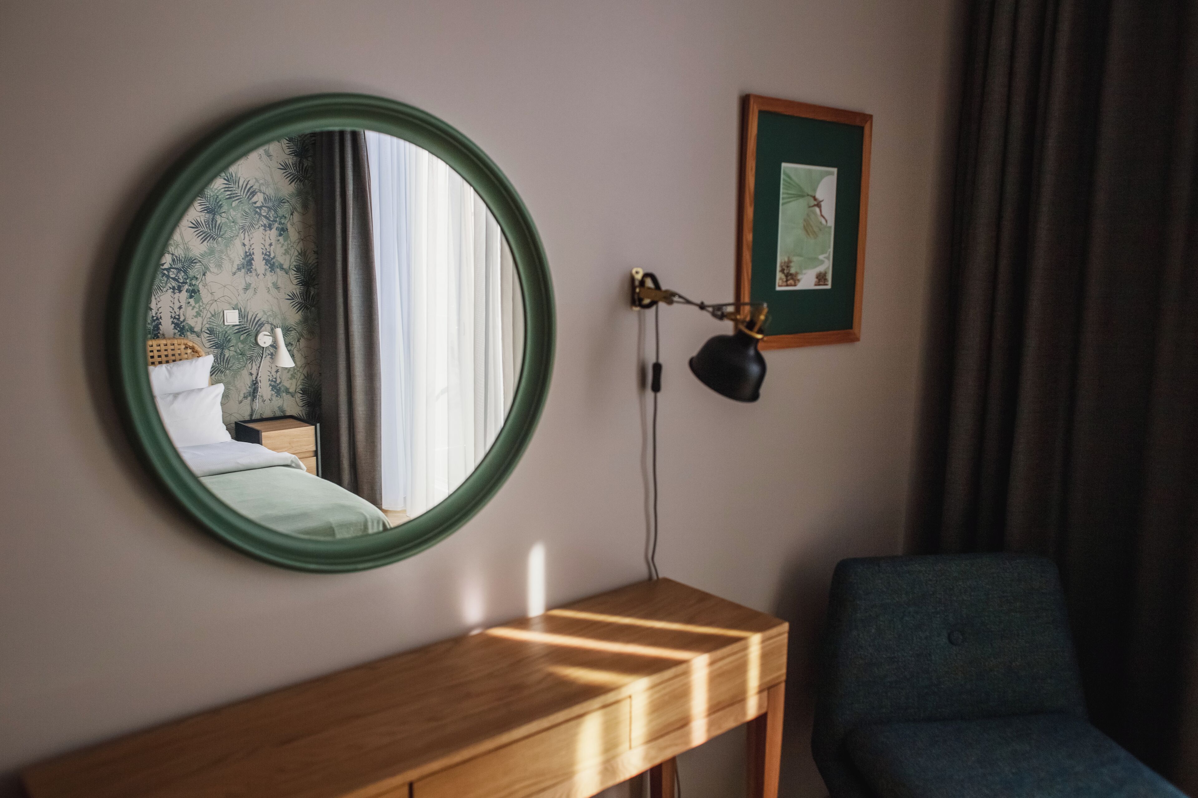 Una habitación con un espejo redondo, una consola de madera, una silla azul, un cuadro enmarco y una lámpara en la pared.