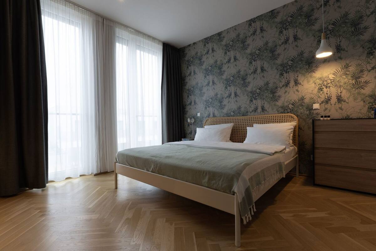 Ein Schlafzimmer mit einem Bett, einem Nachttisch, einer Kommode und einem Fenster mit Vorhängen.