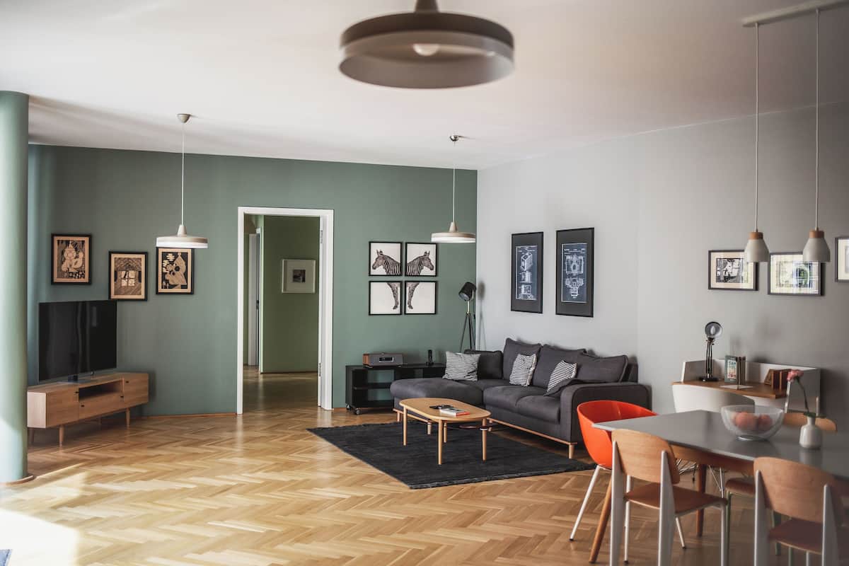 Ein modernes Wohnzimmer mit einer Couch, einem Couchtisch und einem Essbereich. An den Wänden befinden sich Bilderrahmen und ein Fernseher auf einem Schrank.